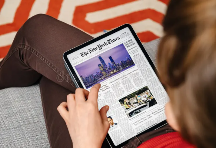 Person reading The New York Times on a tablet, representing the goal to Get featured in The New York Times for increased credibility and media exposure.